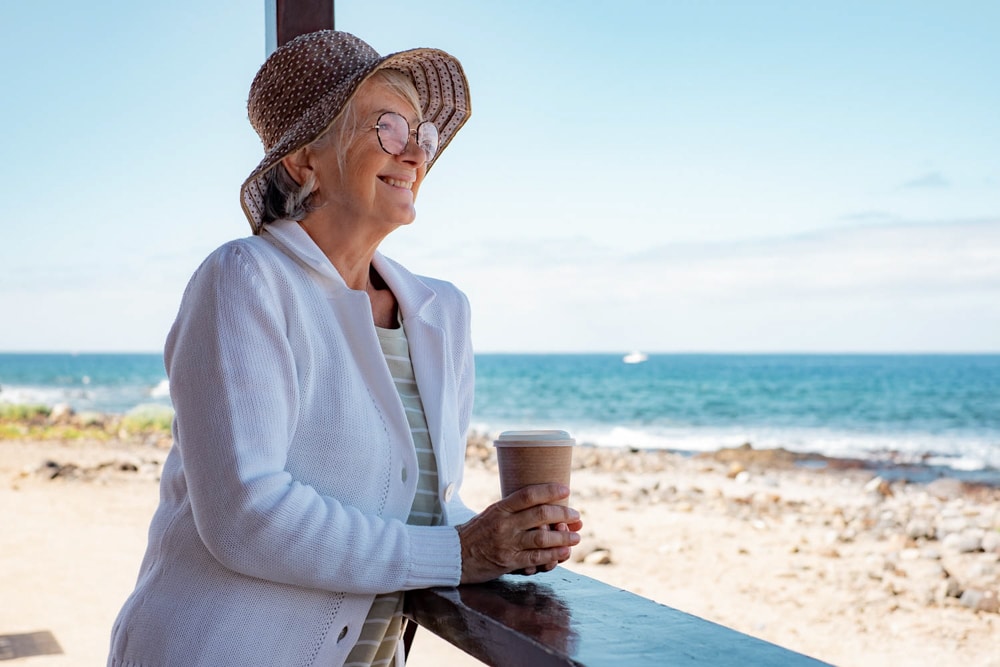 Smiling senior woman in casual clothing with hat and eyeglasses looking at the ocean near largo mobile homes for sale Shoreline Palms